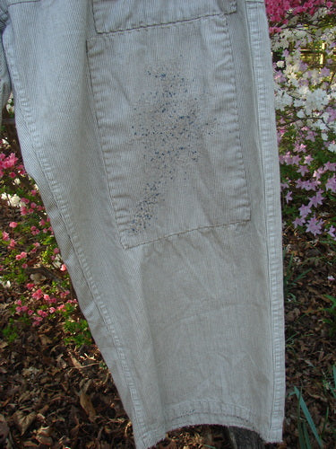 Magnolia Pearl NWT European Denim Lilou Trouser Natural Pinstripe OSFA features a pin-striped leg with a rectangular patch and blue speckles, showcasing distressed, textured stitching. Azalea bushes and fallen leaves form the backdrop.