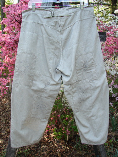 Magnolia Pearl NWT European Denim Lilou Trouser Natural Pinstripe OSFA: loose-fitting, light-beige trousers with adjustable button fly, overlay patches, and distressed details, hanging outdoors against a garden backdrop with flowering shrubs.