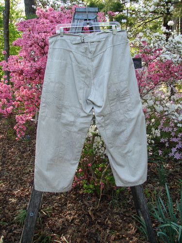 Magnolia Pearl NWT European Denim Lilou Trouser Natural Pinstripe OSFA, hanging on a wooden ladder, showcases adjustable button fly, contrasting patches, raw edges, and textured stitchery against a floral garden backdrop.