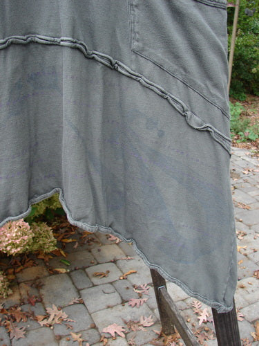 Barclay Cotton Lycra Raw Edge Vector Pocket Tunic, featuring a grey cloth on a pole, a grey blanket on a brick patio, a chair with a blanket on it, and a close-up of a plant.