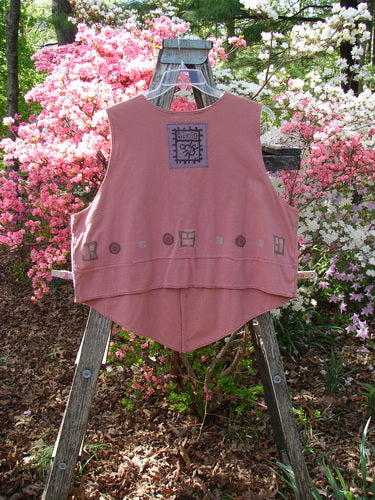 1995 Button Vest Village Russet OSFA draped over a wooden ladder, features geometric motifs, tiny front buttons, and two pockets, set in a rustic garden backdrop with azalea blossoms.