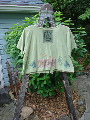 Vintage 1993 Travel Top Beach Treasure Kelp Altered Size 2 on wooden easel, green shirt with beach theme paint, wooden structure, Blue Fish patch. From BlueFishFinder.com's collection of unique, expressive vintage Blue Fish Clothing.