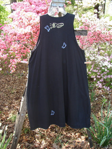 1996 State Fair Vest Music Festival Storm Size 1 features a loose-fitting, sleeveless black jumper with light-blue appliqué designs of musical notes and a bird motif, displayed on a wooden ladder amidst azaleas.