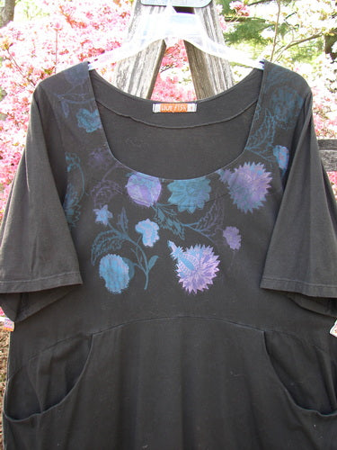 Barclay Short Sleeved Be There Top Floral Bud Black Size 1, featuring a stylized floral print, short sleeves, and front-seam pockets, hanging on a wooden fence.