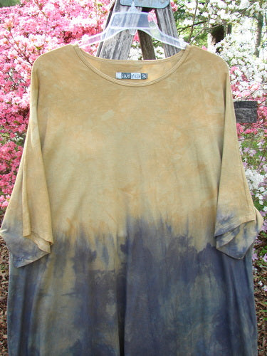 Barclay Art Tunic Tee Mottled Sun Field and Night OSFA hangs on a clear hanger, featuring a sandy tan to deep indigo dip-dye, showcasing its loose fit and unique hemline against azalea blossoms.