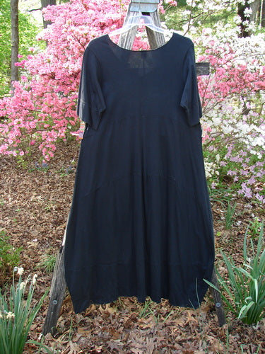 Barclay Gather Sectional Banded Petal Dress Unpainted Black Size 1, featuring short sleeves, a round neckline, and a dippy side hemline, displayed outdoors on a ladder amidst flowering shrubs.