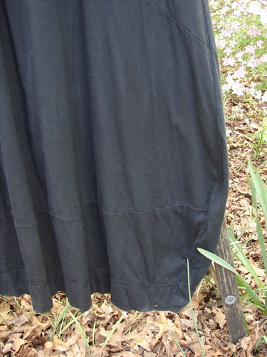 Barclay Gather Sectional Banded Petal Dress in Unpainted Black, Size 1, with a flowing hemline nearly touching dry leaves outdoors, showcasing its sweeping A-line shape and organic cotton texture.
