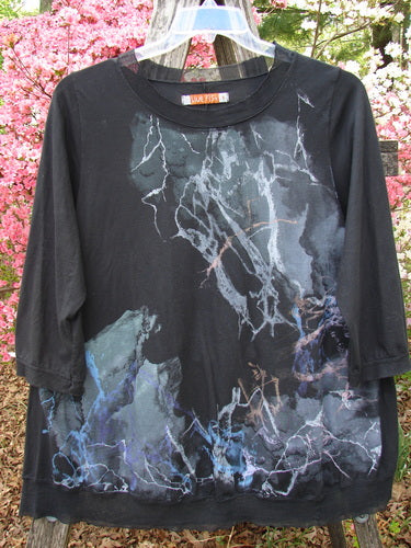 Barclay Flutter Edged Essential Tee, Lightning Black Size 1, features a marbled pattern, three-quarter sleeves, and raw-edged details, hanging outdoors against pink flowering shrubs.