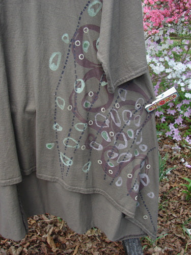 Barclay Hi Low Top Side Art Curly Cue Bark Size 1, featuring a loose, drapey silhouette with hand-painted ovals and dots, drop shoulders, and a scooped neckline, displayed outdoors against blooming azaleas.