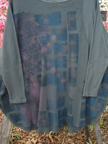 Barclay Thermal Monte Verde Vented Tunic Night Black Army OSFA, featuring abstract rectangular patterns in muted purples and blues, hangs outdoors, showcasing its rounded neckline and side vents.