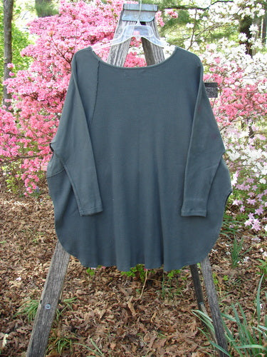 Barclay Thermal Monte Verde Vented Tunic Night Black Army OSFA draped on a wooden ladder, showcasing its oversized, rib-accented sleeves, rounded neckline, and exterior stitchery against a floral backdrop.