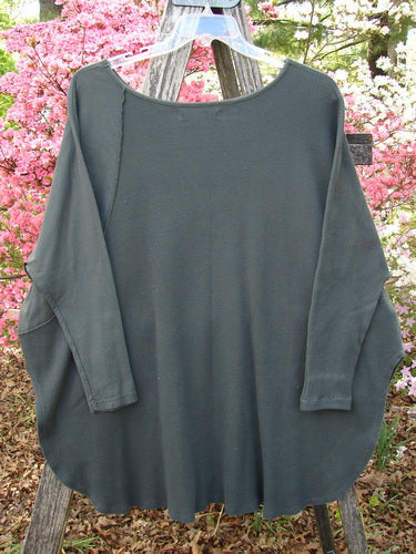 Barclay Thermal Monte Verde Vented Tunic draped on a hanger over an easel, showcasing its loose fit, rounded neckline, and side vents. Features textured fabric and botanical design accents.