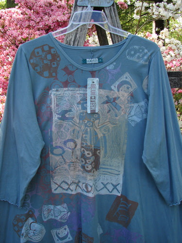 Barclay NWT Color Wheel Tunic Bird Gal Delaware Size 2 features a teal A-line tunic with abstract motifs, three-quarter lettuce-edged sleeves, and a rounded neckline, displayed hanging outdoors on a ladder.