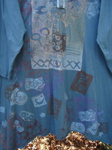 Barclay NWT Color Wheel Tunic Bird Gal Delaware Size 2 displayed outdoors, showcasing abstract motifs of masks, shapes, and leaf-like patterns in muted tones. Features include a rounded neck, three-quarter sleeves, and A-line shape.