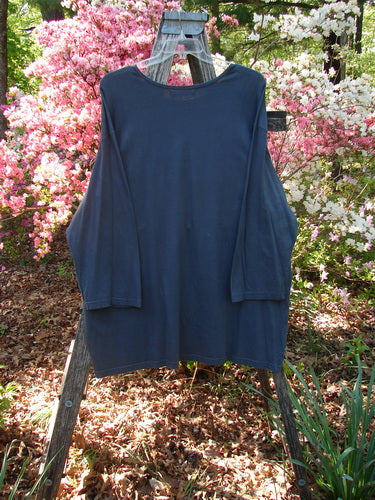 Barclay Long Sleeved Studio Tee Metallic Love Dove Steel Grey OSFA draped over a wooden stepladder, showcasing its loose-fit, long sleeves, rounded neckline, and tunic-style length amidst a garden setting.