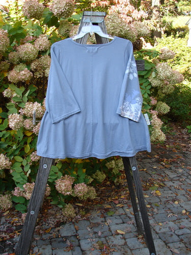 Image: A blue shirt on a rack with plant and flower tags.

Alt text: Barclay Three Quarter Sleeved Crop A Lined Top in Sky Grey, Size 1, on a rack.