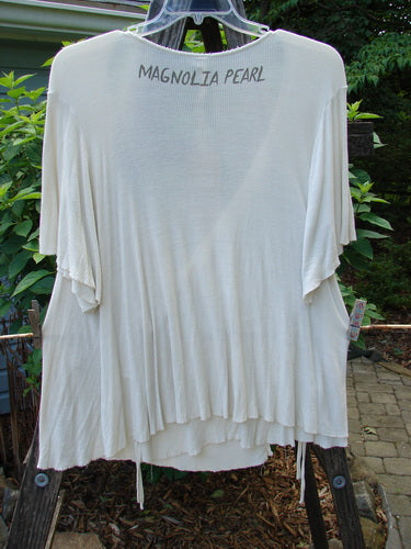 White Magnolia Pearl NWT Ribbed Origami Wrap Blouse with black writing, featuring a deep neckline, three-quarter wide sleeves, two exterior ties, on a clothes rack.