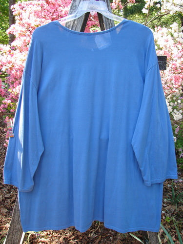 Barclay Long Sleeved Studio Tee Blue Fish Logo Ginger Jar Skylark Size 3, featuring a loose fit, wide neckline, and three-quarter sleeves, hangs against a backdrop of pink and white flowering shrubs.
