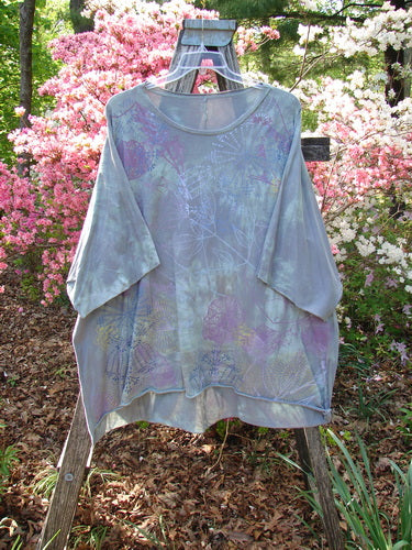 Barclay Flutter Collar Essential Tee Mood Garden Mottled Gray Grass OSFA displayed outdoors, showcasing its rounded flutter neckline, dolman sleeves, and hi-low hemline against a backdrop of azaleas.