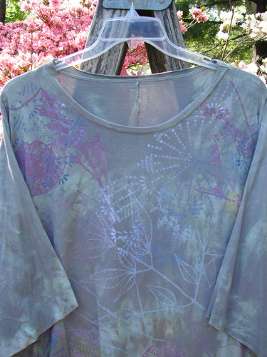 Barclay Flutter Collar Essential Tee Mood Garden Mottled Gray Grass OSFA displayed outdoors, showcasing its semi-sheer fabric with pastel floral prints, flutter neckline, and raw edge details.