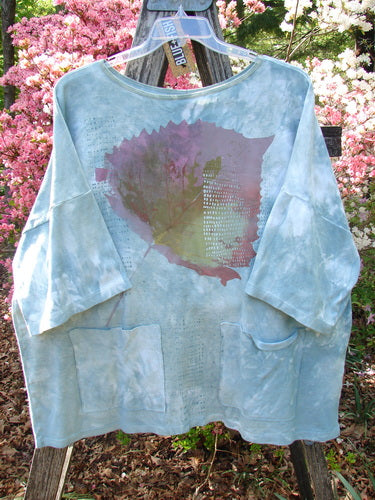 Barclay NWT Cotton Lycra Writer's Pocket Pullover Sweatshirt Leaf Mottled Asper OSFA, oversized with abstract leaf graphic and dual pockets, displayed outdoors on a wooden frame against flowering shrubs.