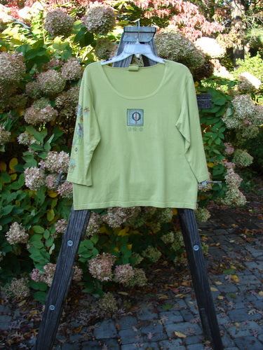 A Barclay Three Quarter Sleeved Deep Neck Tee in Citron, Size 1, featuring a green shirt on a swinger with a rack in the background.
