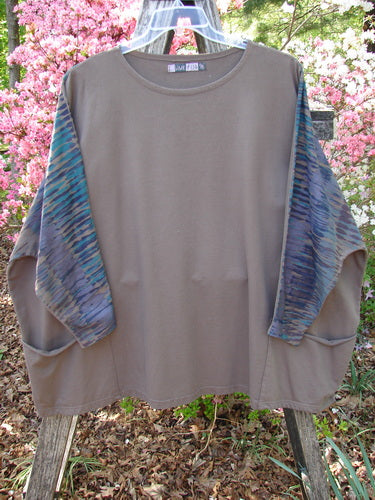 Barclay Cotton Lycra Writer's Pocket Pullover Sweatshirt Rear Rain Dark Bark OSFA: A taupe tunic with vibrant striped sleeves, dual front pockets, and seamless design, hanging outdoors against blooming azaleas.