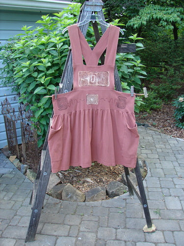 1995 Overall Jumper Stone Path Russet OSFA displayed on a wooden frame, featuring crisscross back straps, oversized side pockets, and a full gathered skirt, showcasing the creative bib design and signature Blue Fish patch.