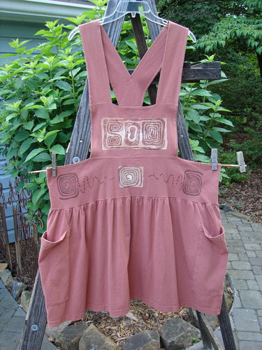 1995 Overall Jumper Stone Path Russet OSFA displayed on a wooden fence, featuring a creatively cut bib, crisscross back straps, oversized side pockets, and a full gathered skirt with a classic stone path theme.