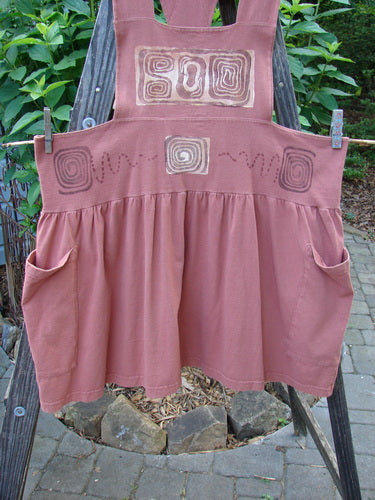 1995 Overall Jumper Stone Path Russet OSFA displayed on a wooden stand, featuring a creatively cut bib, crisscross back straps, oversized pockets, and a full gathered playful skirt.