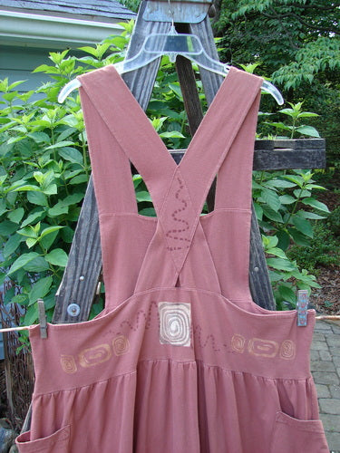 1995 Overall Jumper Stone Path Russet OSFA hanging on a clothesline, featuring a creatively cut bib, shorter length, full gathered skirt, oversized side pockets, crisscross back straps, and a double-stitched waist panel.