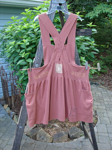 1995 Overall Jumper Stone Path Russet OSFA on a wooden rack, showcasing its creatively cut bib, full gathered skirt, oversized side pockets, and crisscross back straps.