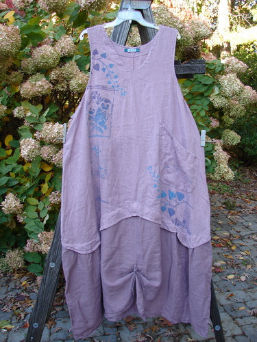 Barclay PMU Linen Explorer Jumper in Lavender, size 2. A purple dress on a wooden rack. Close-up of dress details and metal object.