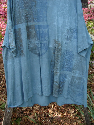 Barclay Art Tunic Tee Cosmic Celtic Steel Blue OSFA: A loose-fitting, slate-blue tunic with geometric motifs, drop shoulders, and a varying hemline, draped on a wooden support.