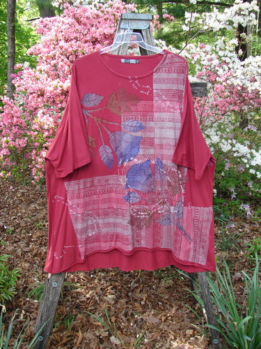 Barclay Art Tunic Tee Trailing Floral Deep Ruby OSFA, displayed on a wooden ladder in a garden, features patchwork stripes, a dove motif, and three-quarter sleeves in medium-weight organic cotton.