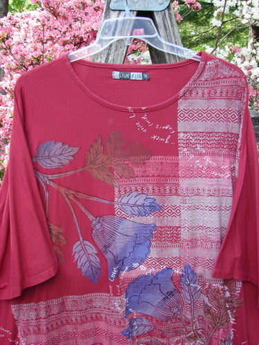 Barclay Art Tunic Tee Trailing Floral Deep Ruby OSFA features a mix of tribal stripes and botanical prints, drop shoulders, loose three-quarter sleeves, and a rounded neckline hanging on a clear plastic hanger.