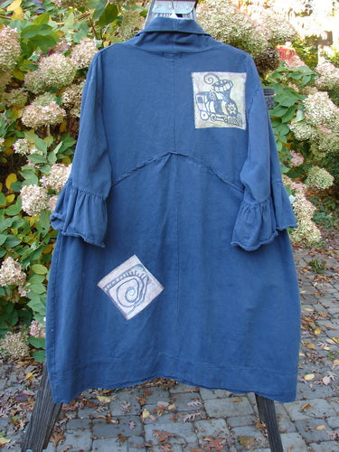 A Barclay PMU Patched Twill Decora Brushed Flutter Coat in Navy. A blue dress with a picture on it, featuring a blue design and a white square with a spiral design. Also includes a drawing of a train and a blue blanket on a brick surface.