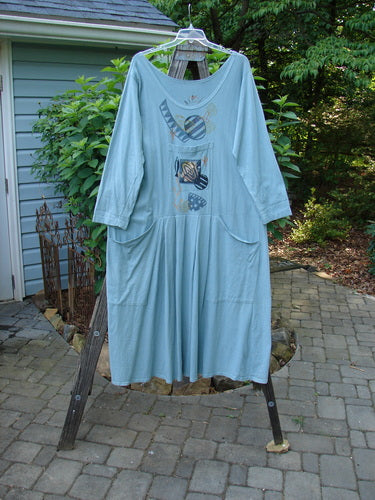 1995 Farmer Jen Dress Fish Atom Dinette Green Size 1 displayed hanging on a clothesline, showcasing its longer cozy sleeves, deeper rounded neckline, and multiple front pockets against an outdoor backdrop.