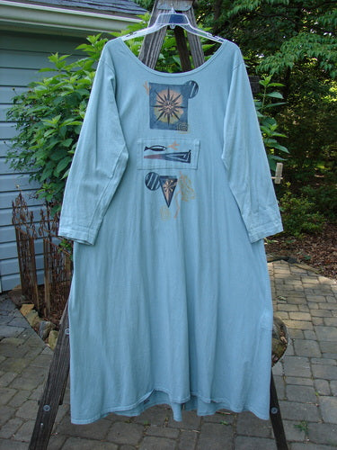 1995 Farmer Jen Dress Fish Atom Dinette Green Size 1 hanging on a clothesline, showcasing its rounded neckline, longer sleeves, upper center pocket, lower tunnel pocket, deep front cargo pockets, and unique atom theme design.