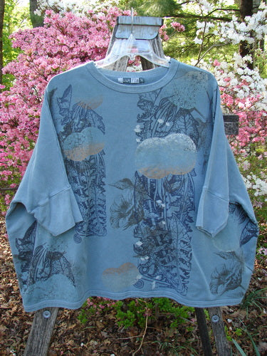 Barclay Fleece Banded Sleeve Dolman Top Moon Garden Sage OSFA, displayed outdoors on a hanger, features a slate-blue hue with a botanical/cloud print, showcasing its wide, boxy shape and banded sleeves.
