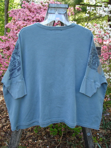 Barclay Fleece Banded Sleeve Dolman Top Moon Garden Sage Dust OSFA draped over a ladder, showcasing its wide boxy shape and banded sleeve details against a backdrop of blooming azaleas.