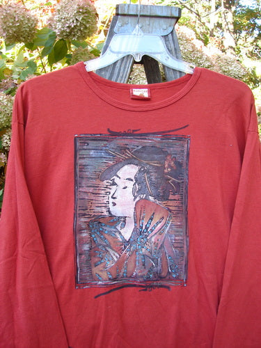 A red shirt with a picture on it, featuring a Geisha Gal theme paint. The Barclay Long Sleeved Tee from the Fall Collection in Geisha's Robe is made from Organic Cotton. It has a rounded neckline, long cozy sleeves, and a wide slightly longer shape. Perfect Condition. Size 1.