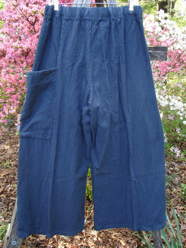Barclay Heavy Linen Single Side Pocket Pant in Unpainted Navy features a loose-fit, wide-leg design with an elastic waistband and a single patch pocket, hanging outdoors against blooming shrubs.