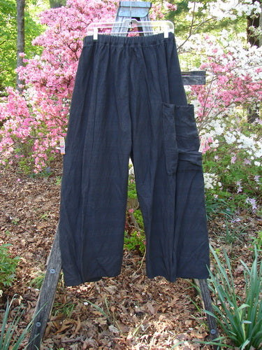 Barclay Linen Striation Single Side Pocket Pant in Unpainted Black, loose-fitting, displayed on a hanger. Features include full elastic waist, single exterior side pocket, longer inseam, and light striation.