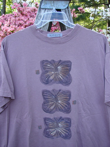 1996 Short Sleeved Tee Triple Butterfly Petal Size 2 features three stylized butterflies down its front. Hanging outdoors, the mauve-purple tee showcases a thicker ribbed neckline and a lengthier boxy shape.
