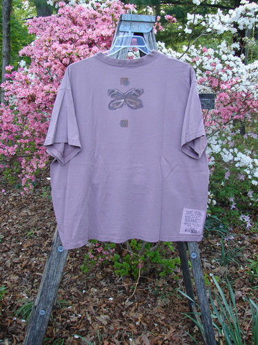 1996 Short Sleeved Tee Triple Butterfly Petal Size 2 displayed on a wooden ladder, showcasing a butterfly graphic and a sewn-on patch, set against blooming azaleas, epitomizing vintage Blue Fish creativity.