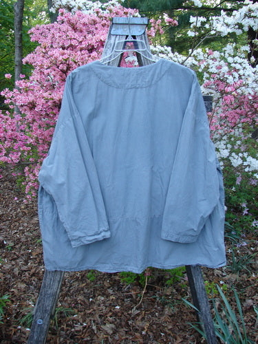 2000 Percal Overshirt Top Unpainted Eucalyptus Size 2 displayed on a wooden easel frame, showcasing its loose, airy fit with drop shoulders and a softly rounded V-neckline amidst a garden backdrop.