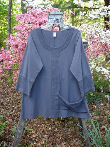 Barclay Cotton Lycra Celtic Moss Single Pocket Tunic Unpainted Grey Plum Size 1, displayed on a wooden ladder, features a scoop neckline, three-quarter sleeves, and distinctive Celtic Moss accents in a garden setting.