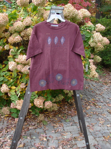 1997 Short Sleeved Tee Triple Leaf Stained Glass Size 1: A red and purple shirt with leaves on a rack and wooden stand.