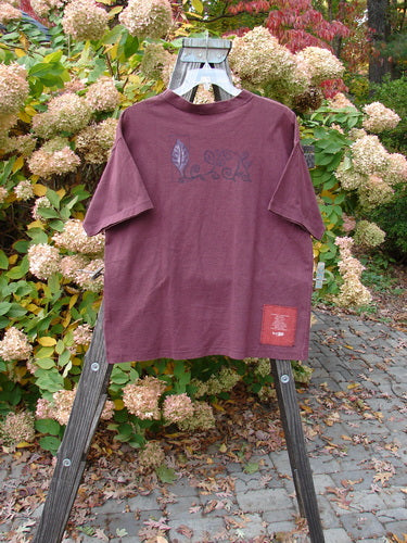 1997 Short Sleeved Tee Triple Leaf Stained Glass Size 1: A red t-shirt with a logo on a wooden rack.